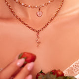 Necklace with heart pendant held by a person, with strawberries in the background