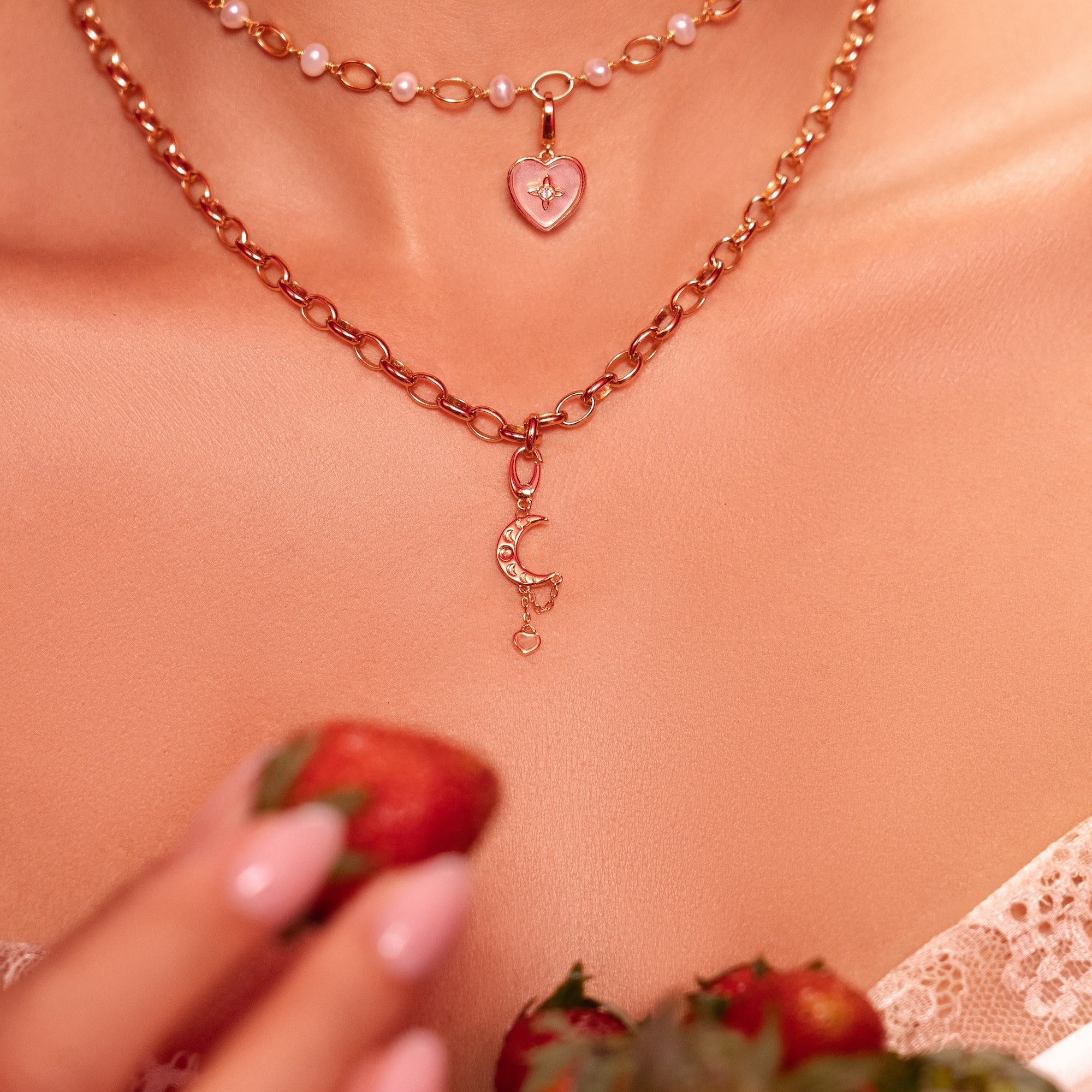 Necklace with heart pendant held by a person, with strawberries in the background