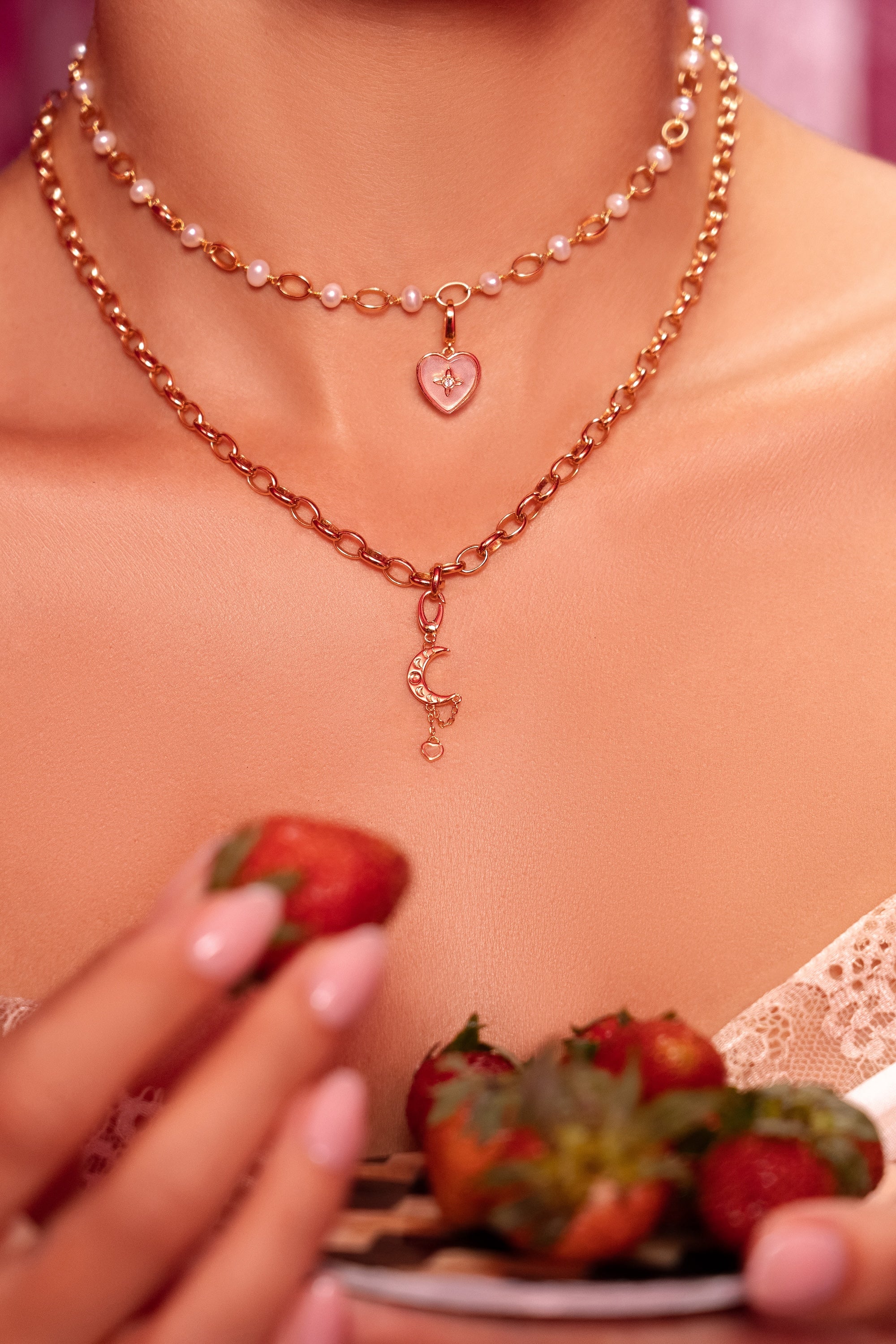 Necklace with heart pendant held by a person, with strawberries in the background