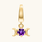 A gold triple moon pendant charm featuring a central round-cut purple amethyst gemstone, set against a plain off-white background.