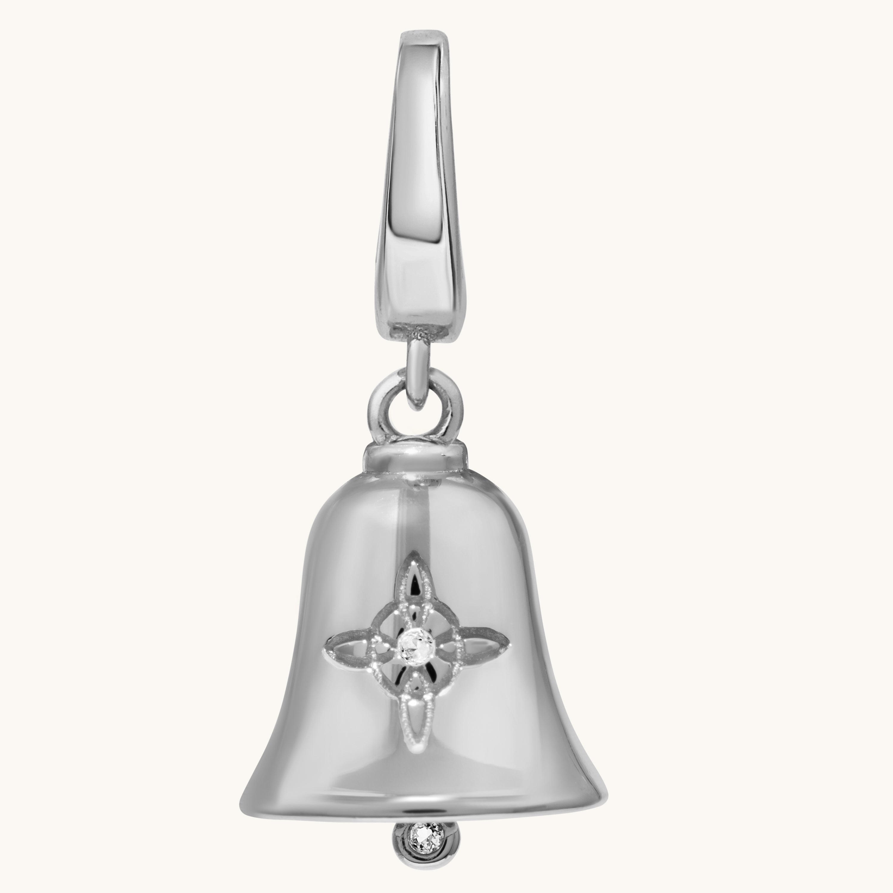 Close-up of a silver bell charm with a Witch’s Knot engraved on its polished surface on a ight cream background.