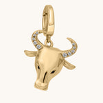 Gold bull head charm with stone encrusted eyes and horns on a white background