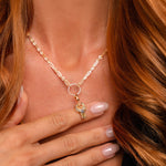 A woman with long red hair wears the Preorder: Odin Charm (Ships end October 2026), its Norse mythology pendant resting on her chest. Her manicured hand touches the charm, complementing her black top.