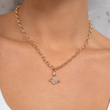 A close-up of a model wearing a delicate gold chain necklace with a small pendant featuring a clear central gemstone.