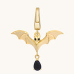Gold bat charm with outstretched sculpted wings, dark eyes, and a dangling black stone.