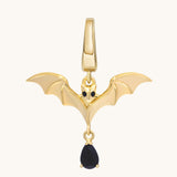 Gold bat charm with outstretched sculpted wings, dark eyes, and a dangling black stone.