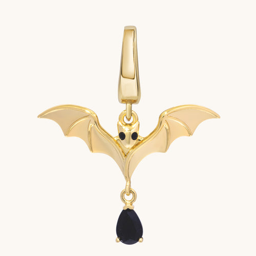 Gold bat charm with outstretched sculpted wings, dark eyes, and a dangling black stone.