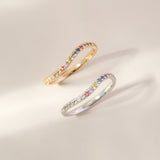 Two rings, one gold and one silver, with colorful gemstones on a light beige background.