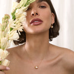 Woman holding flowers with a gold  Cauldron necklace against a white background