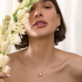 Woman holding flowers with a gold  Cauldron necklace against a white background