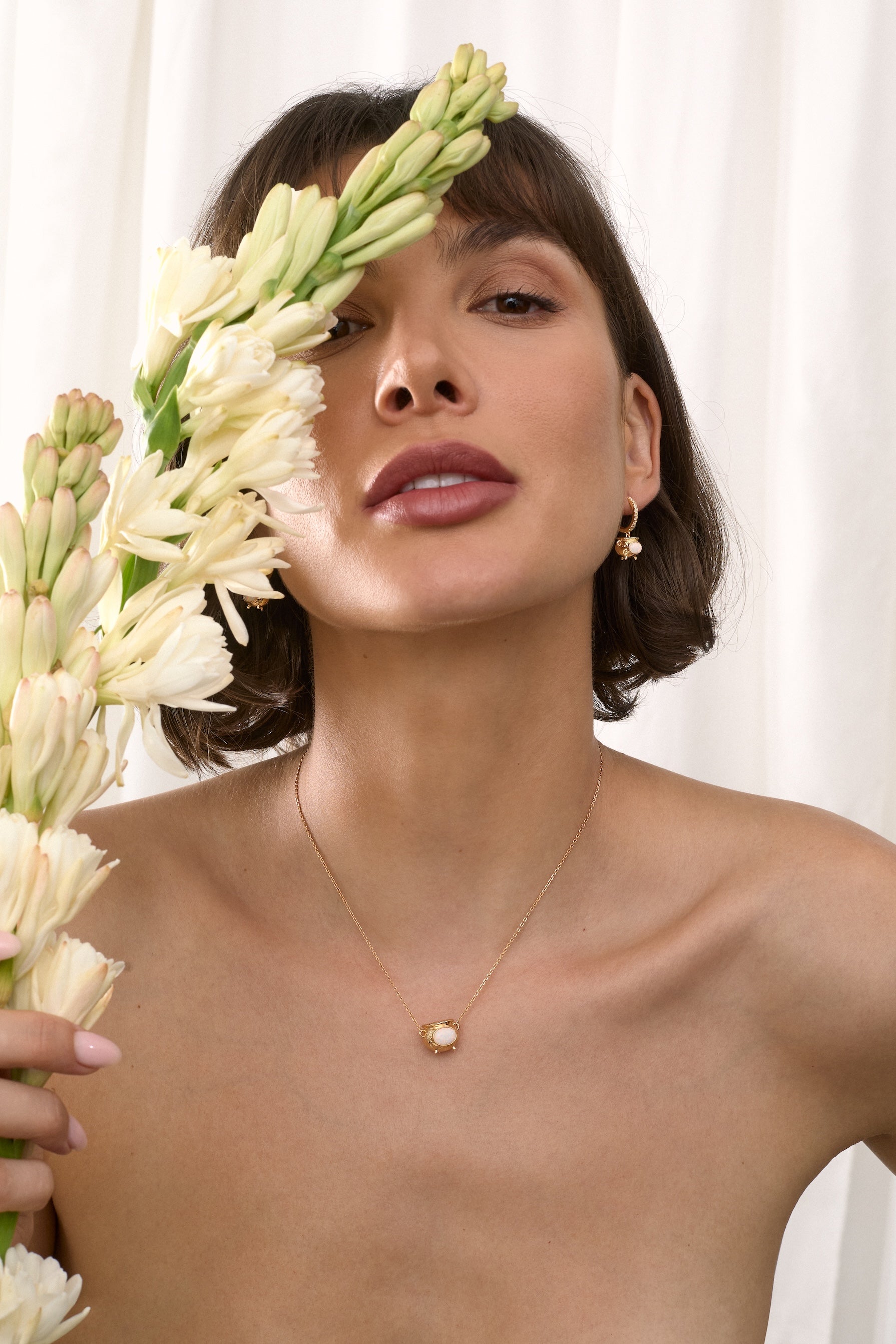 Woman holding flowers with a gold  Cauldron necklace against a white background
