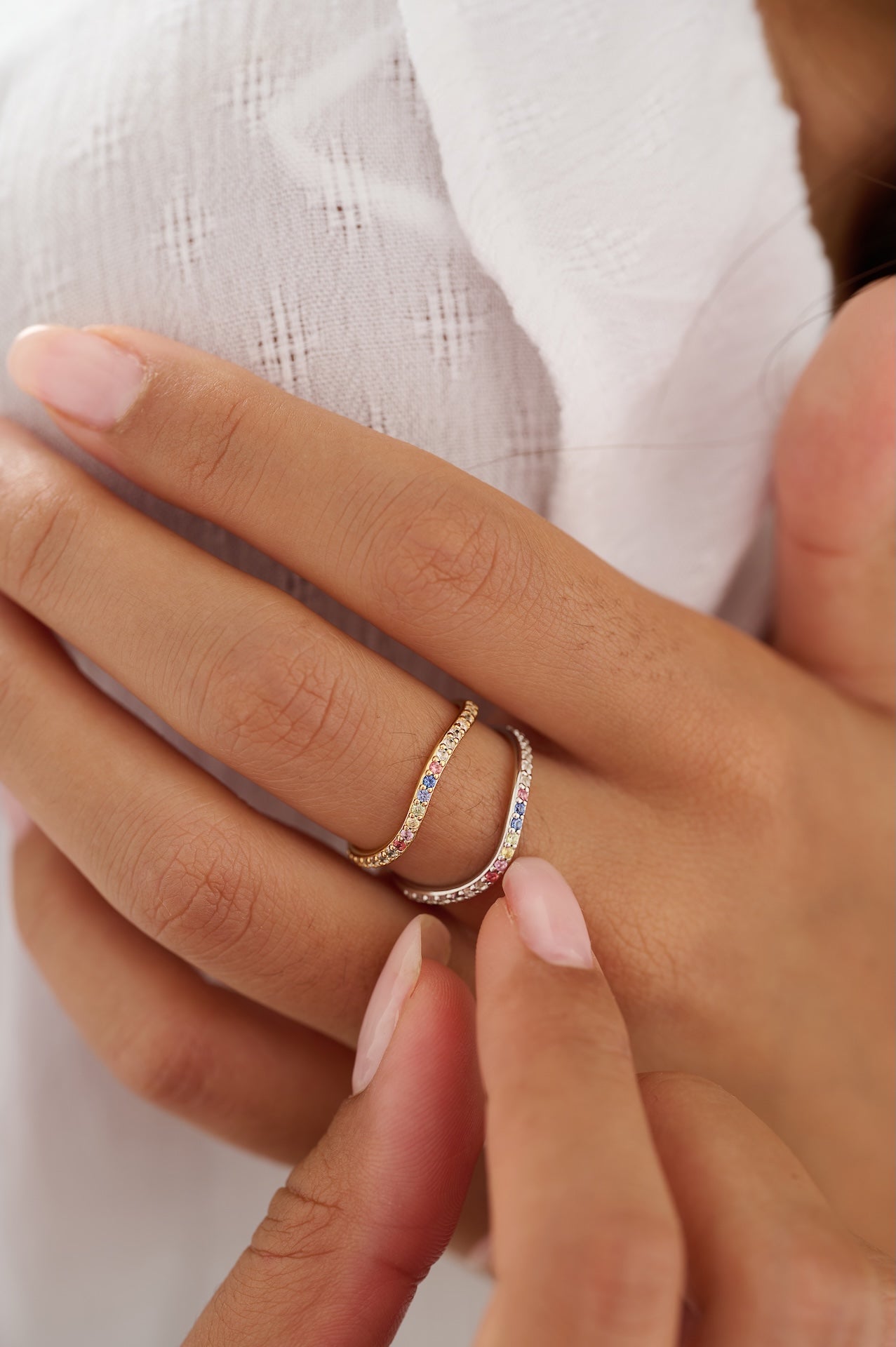 Close-up of a hand wearing two gold rings with gemstones on a white background