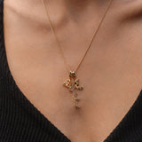 Close-up of a person wearing a gold necklace with three charms: a triquetra symbol, a script ‘magickal’ charm, and a gold crescent moon with black and white stones.