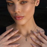 Woman wearing a gold crescent moon necklace, gold pentacle stud earrings, and a gold Triquetra ring with an intricate design.