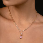 A close-up of a model wearing a delicate rose gold chain necklace with a small pomegranate pendant featuring pink gemstones, set against a dark background.