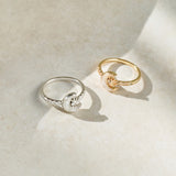 Two crescent moon-shaped rings, one silver and one gold, on a light beige surface.