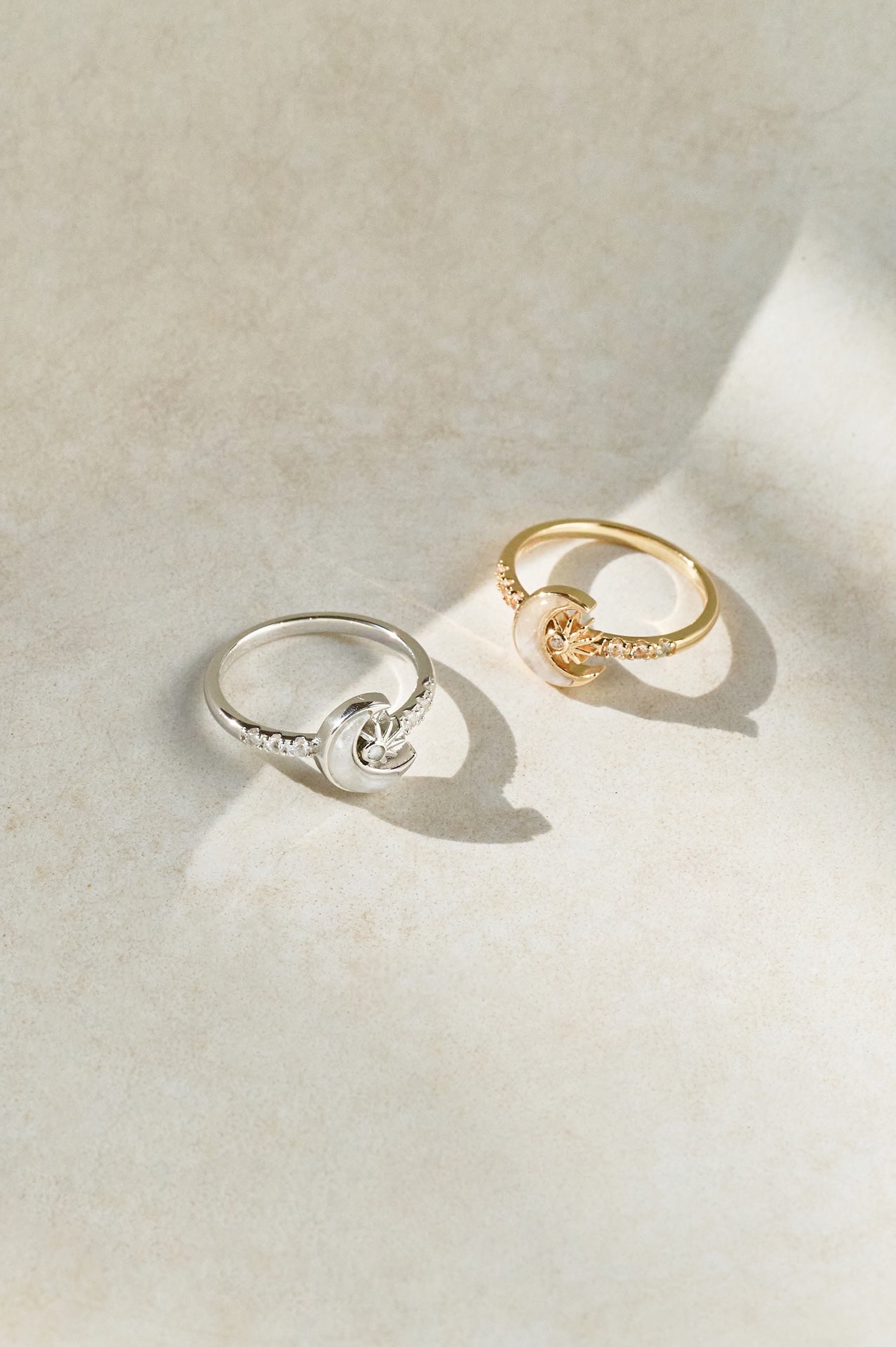 Two crescent moon-shaped rings, one silver and one gold, on a light beige surface.