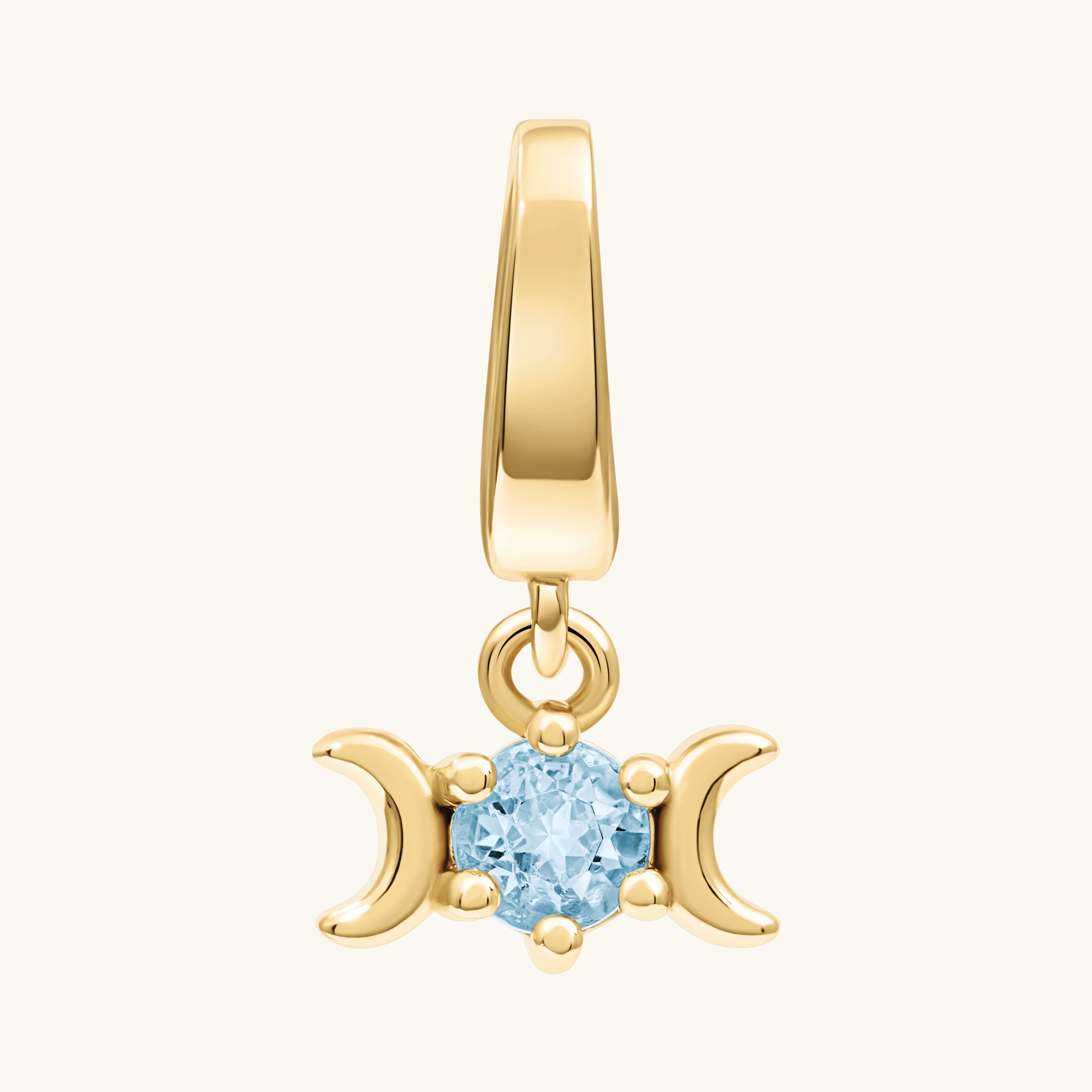 A gold pendant charm featuring a triple moon symbol surrounding a round light blue gemstone, shown on a light cream background.