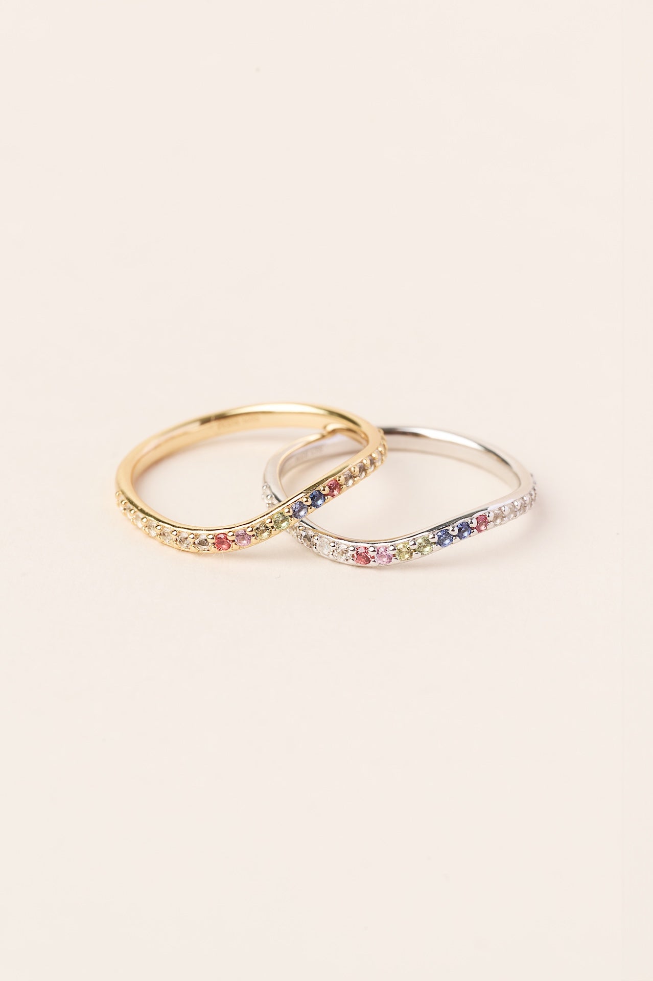 Two rings with colorful gemstones on a light beige background