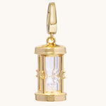 A polished silver hourglass pendant charm with a clear glass center and glittering crystal-toned sand inside, shown on a light cream background.