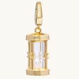 A polished silver hourglass pendant charm with a clear glass center and glittering crystal-toned sand inside, shown on a light cream background.