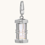 A polished silver hourglass pendant charm with a clear glass center and glittering crystal-toned sand inside, shown on a light cream background.