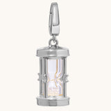 A polished silver hourglass pendant charm with a clear glass center and glittering crystal-toned sand inside, shown on a light cream background.
