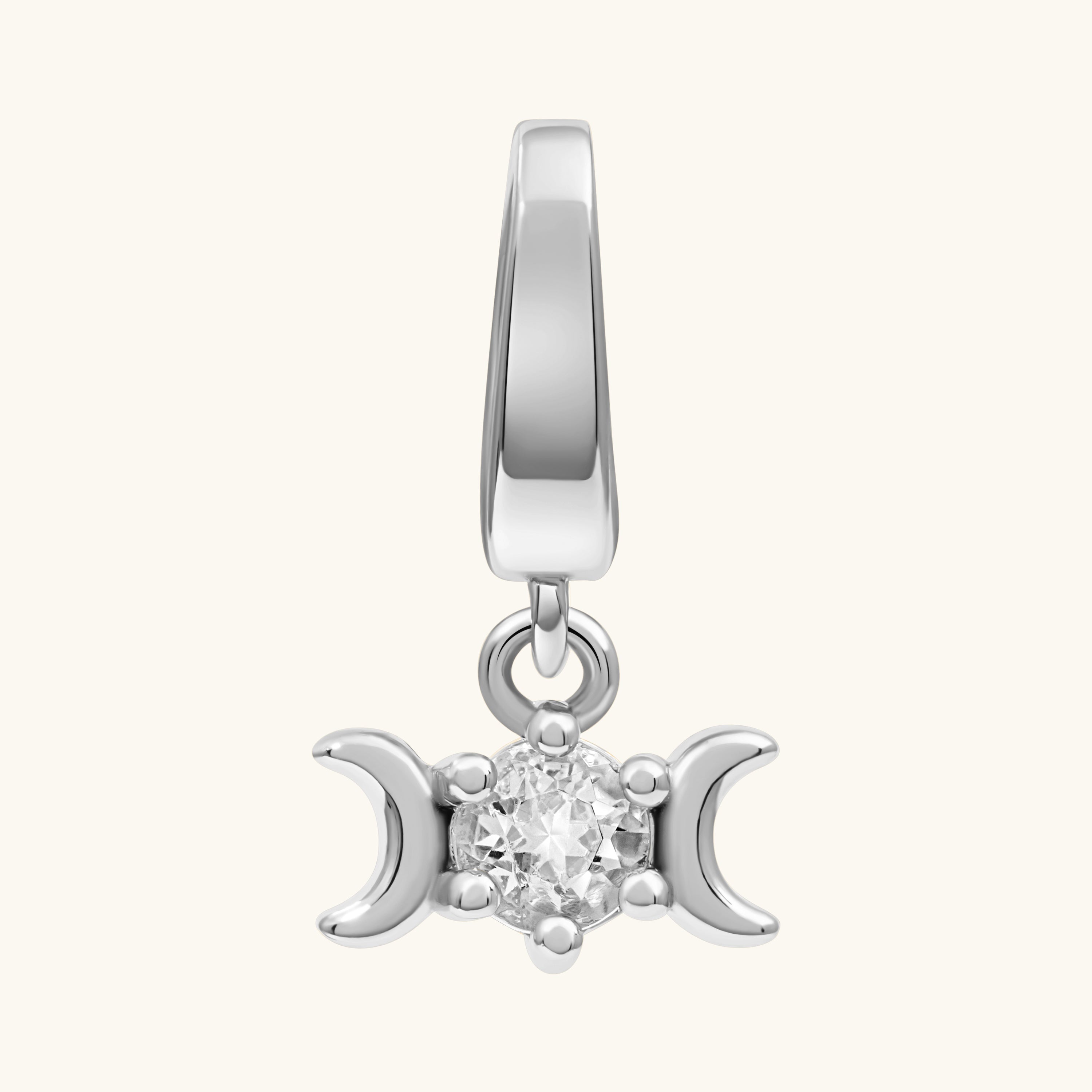 A silver-toned triple moon charm pendant featuring a central clear gemstone, set against a solid off-white background.