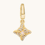 A gold-toned charm pendant featuring a central pale moonstone gemstone surrounded by clear white topaz stones, suspended from a matching gold bail, shown on a light cream background.
