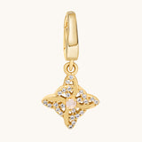 A gold-toned charm pendant featuring a central pale moonstone gemstone surrounded by clear white topaz stones, suspended from a matching gold bail, shown on a light cream background.