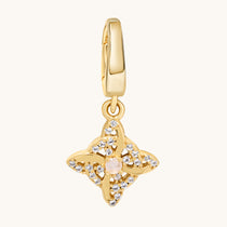 A gold-toned charm pendant featuring a central pale moonstone gemstone surrounded by clear white topaz stones, suspended from a matching gold bail, shown on a light cream background.