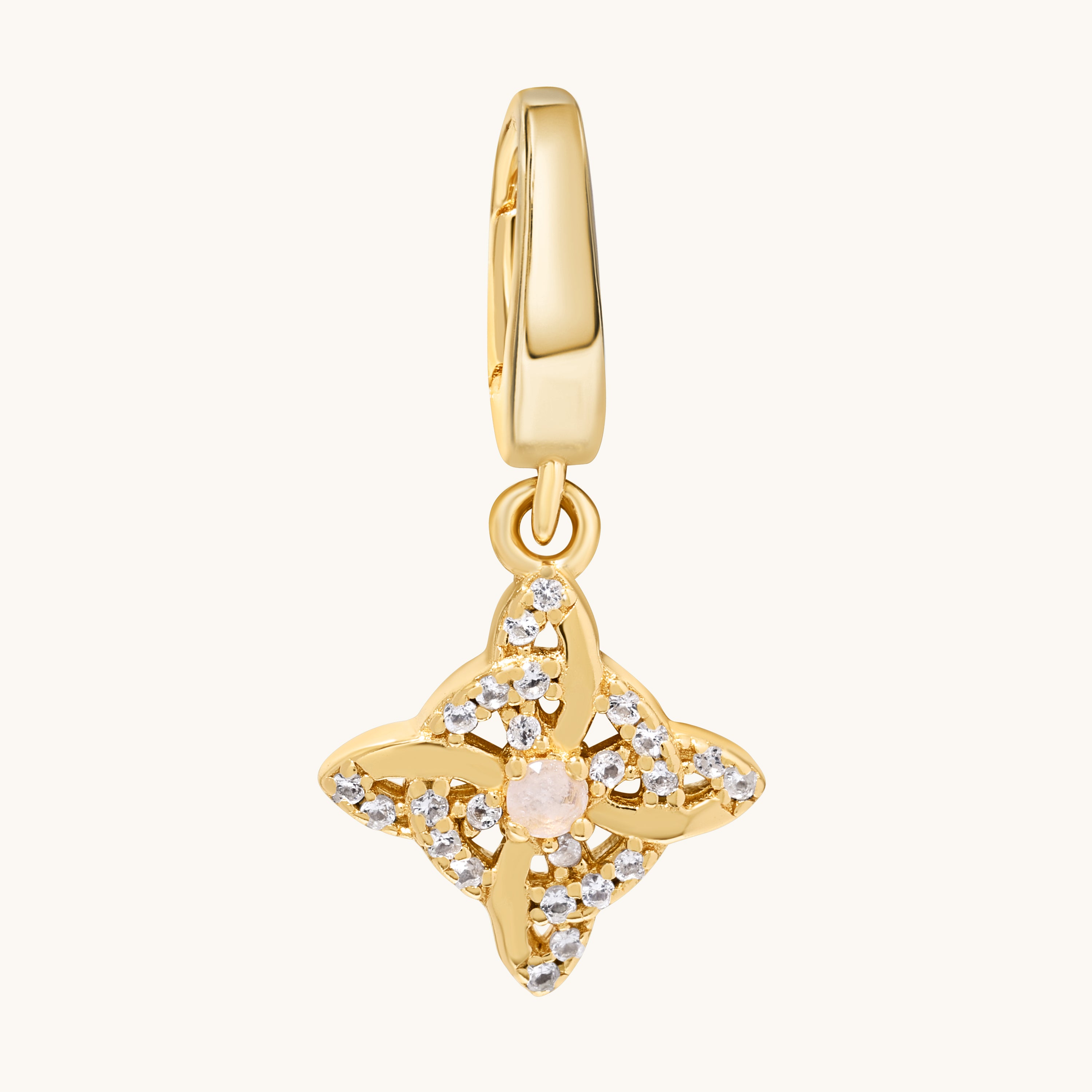 A gold-toned charm pendant featuring a central pale moonstone gemstone surrounded by clear white topaz stones, suspended from a matching gold bail, shown on a light cream background.