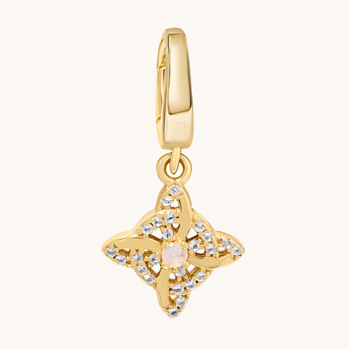 A gold-toned charm pendant featuring a central pale moonstone gemstone surrounded by clear white topaz stones, suspended from a matching gold bail, shown on a light cream background.