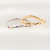 Two rings, one with colorful gemstones and the other gold, on a white background