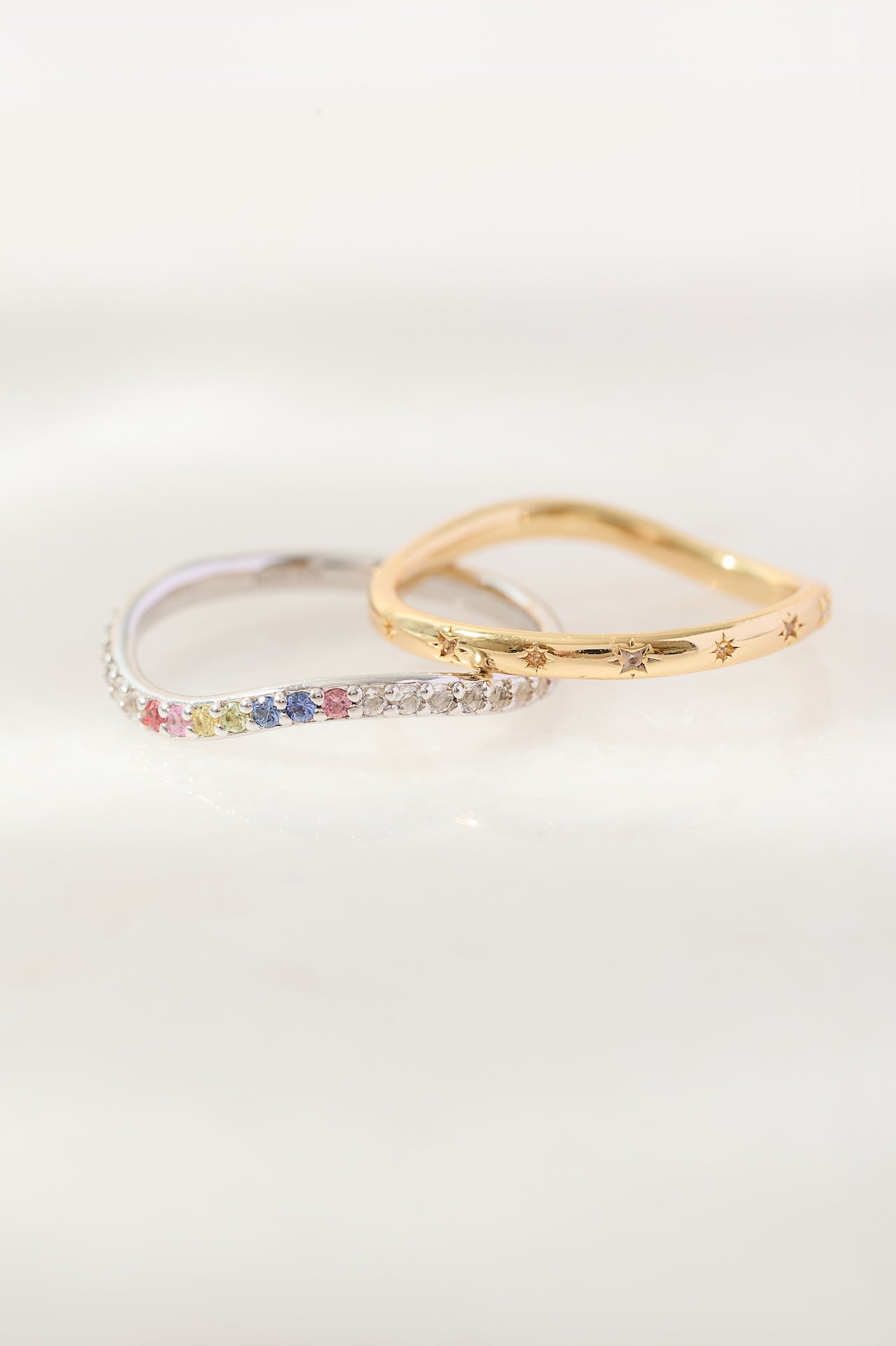 Two rings, one with colorful gemstones and the other gold, on a white background