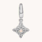 A silver-toned charm pendant featuring a central pale moonstone gemstone surrounded by clear white topaz stones, suspended from a matching silver bail, shown on a light cream background.