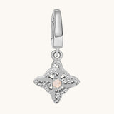 A silver-toned charm pendant featuring a central pale moonstone gemstone surrounded by clear white topaz stones, suspended from a matching silver bail, shown on a light cream background.