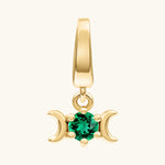 A gold triple moon pendant charm featuring a central round-cut green gemstone, set against a plain off-white background.