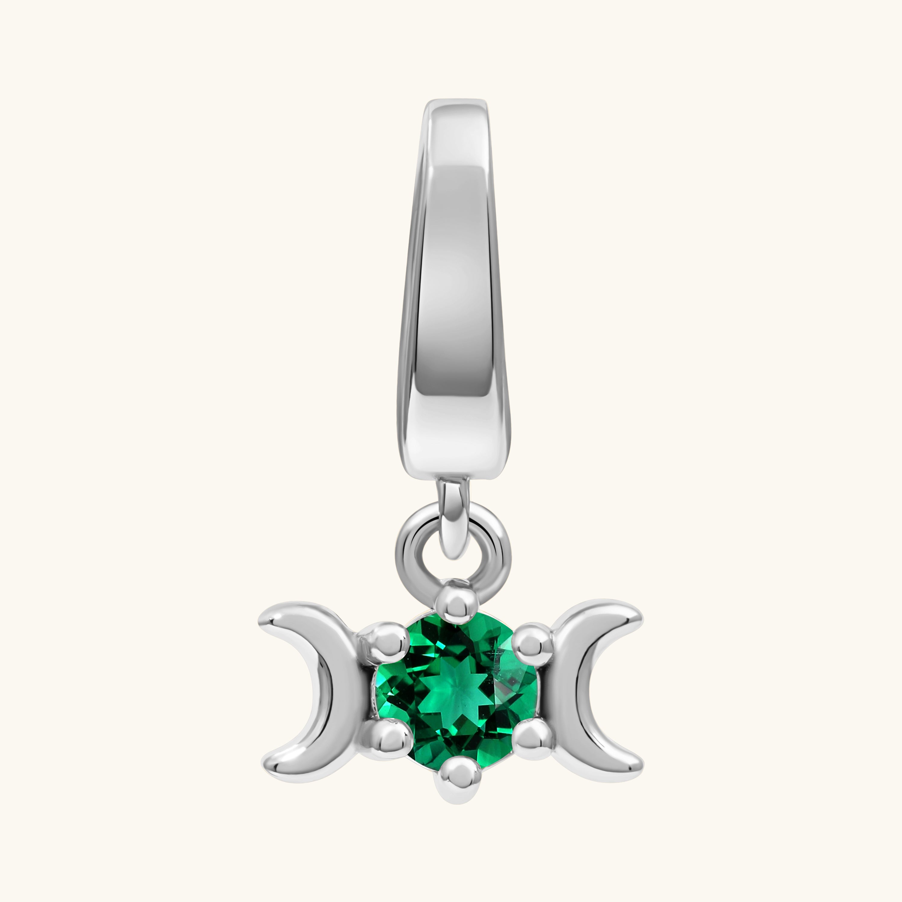 A sterling silver triple moon pendant charm featuring a central round-cut green gemstone, set against a solid off-white background.