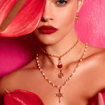 Close-up of a person wearing rose gold necklaces with red flowers in the foreground.