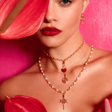 Close-up of a person wearing rose gold necklaces with red flowers in the foreground.