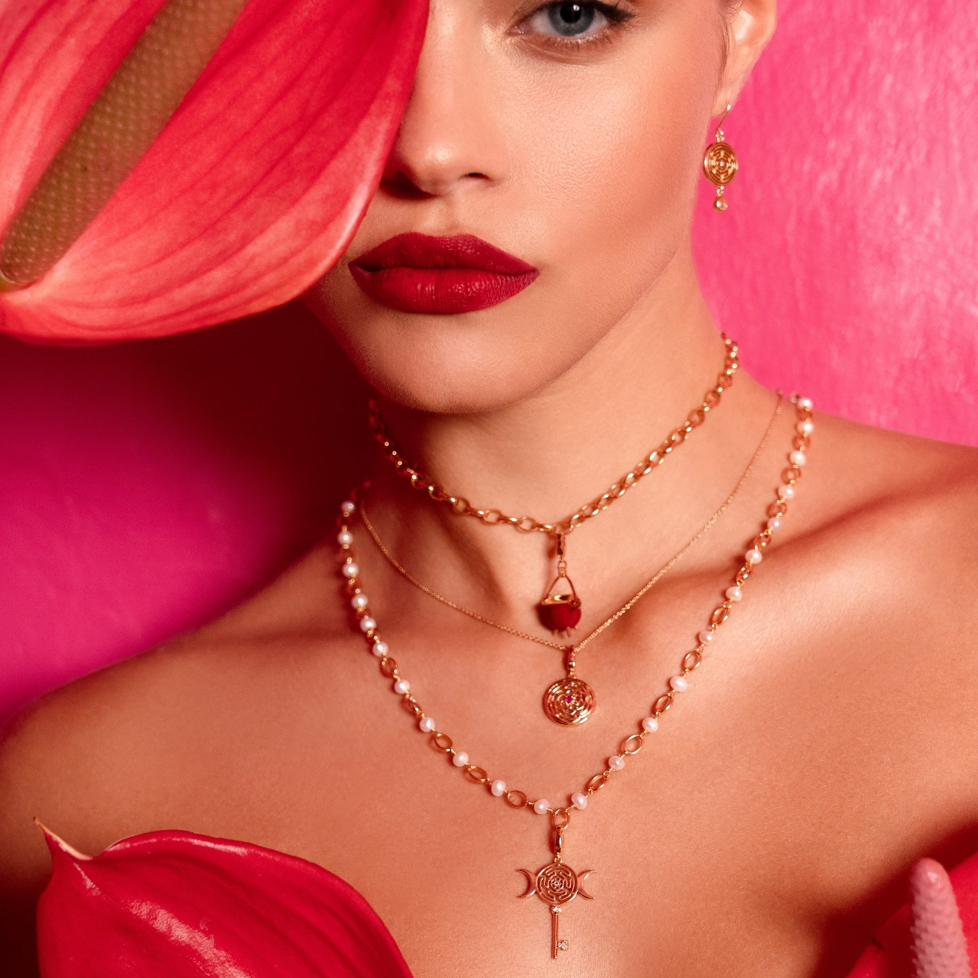 Close-up of a person wearing rose gold necklaces with red flowers in the foreground.
