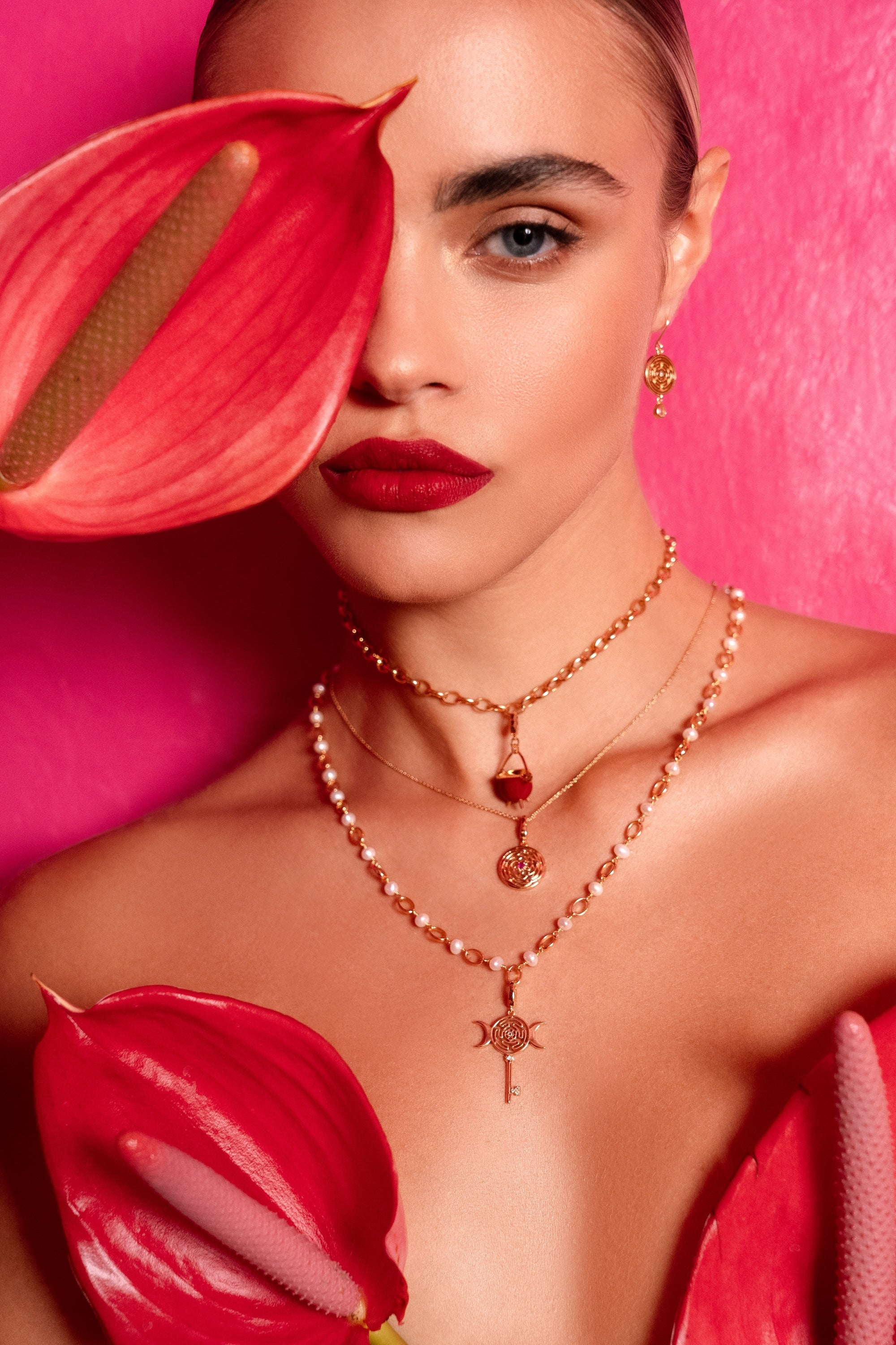 Close-up of a person wearing rose gold necklaces with red flowers in the foreground.