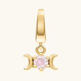 A gold triple moon pendant charm featuring a central round light white moonstone gemstone, set against a solid off-white background.