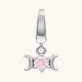 A silver-toned triple moon charm pendant featuring a central round pink gemstone, shown against a solid off-white background.