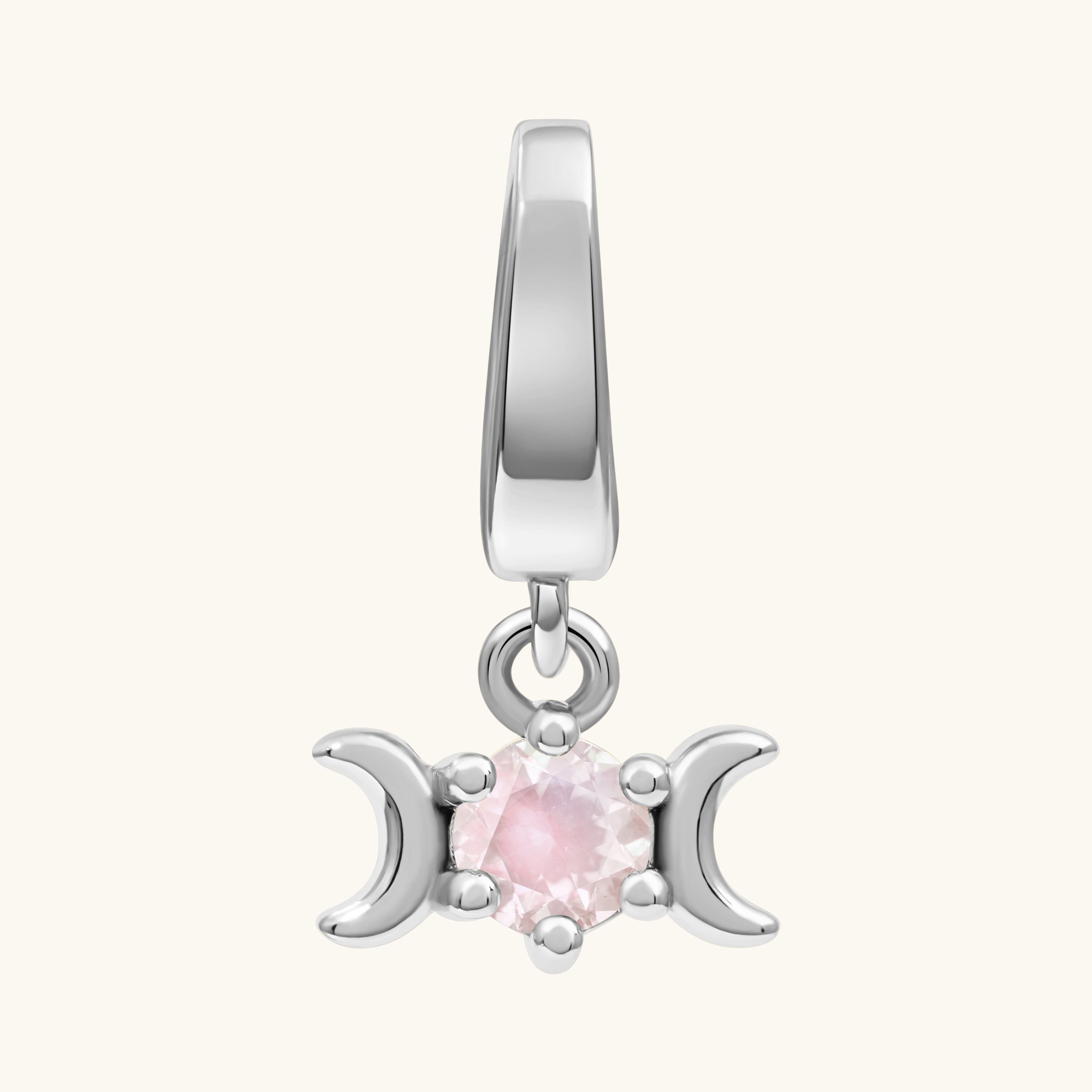 A silver-toned triple moon charm pendant featuring a central round pink gemstone, shown against a solid off-white background.