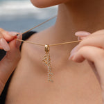 Close-up of a person holding a gold necklace with two charms: a triquetra symbol and a script ‘magickal’ charm