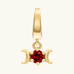A gold triple moon pendant charm featuring a central faceted red gemstone, set against a plain off-white background.