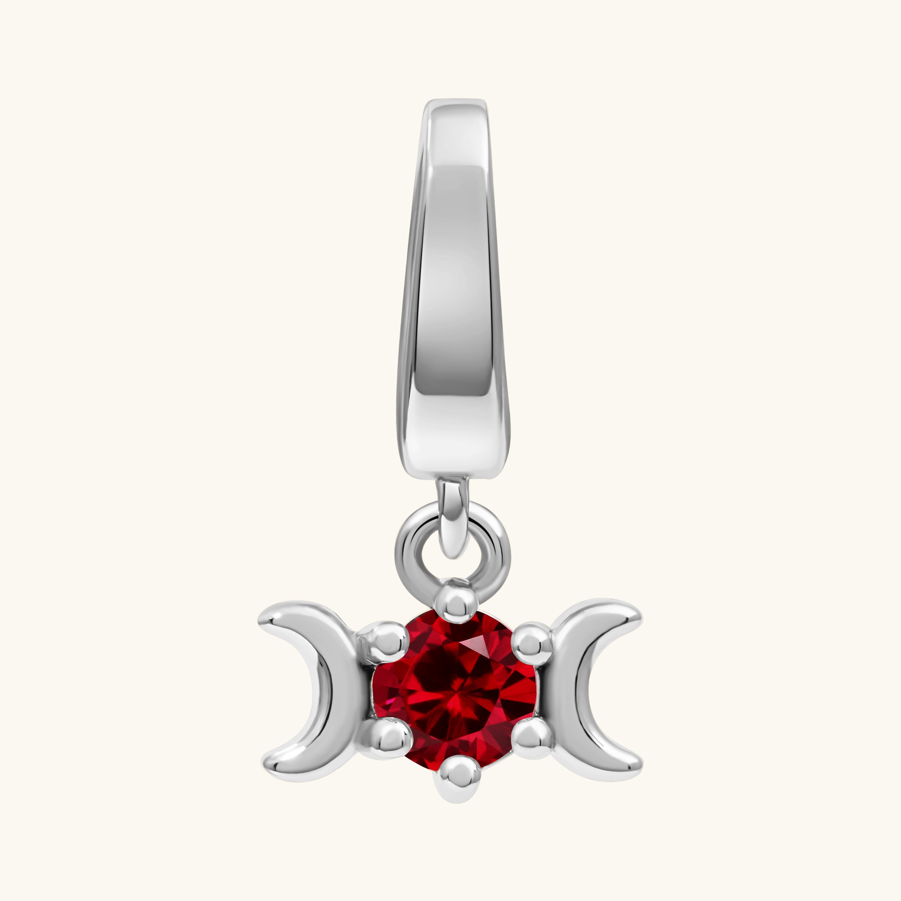 A silver-toned triple moon pendant charm featuring a central faceted red gemstone, set against a solid off-white background.