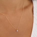 Gold necklace with a small pendant on a person wearing a white top.